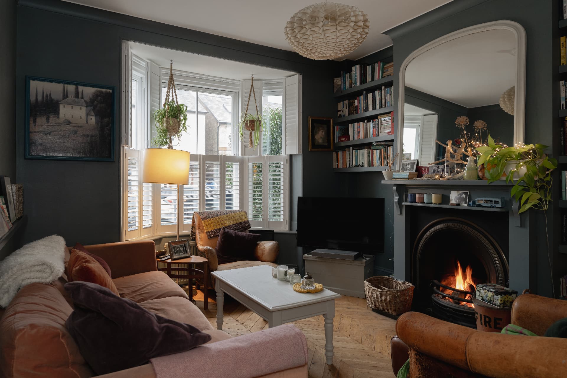 A welcoming living room with a lit fireplace, velvet sofas and built-in bookshelves