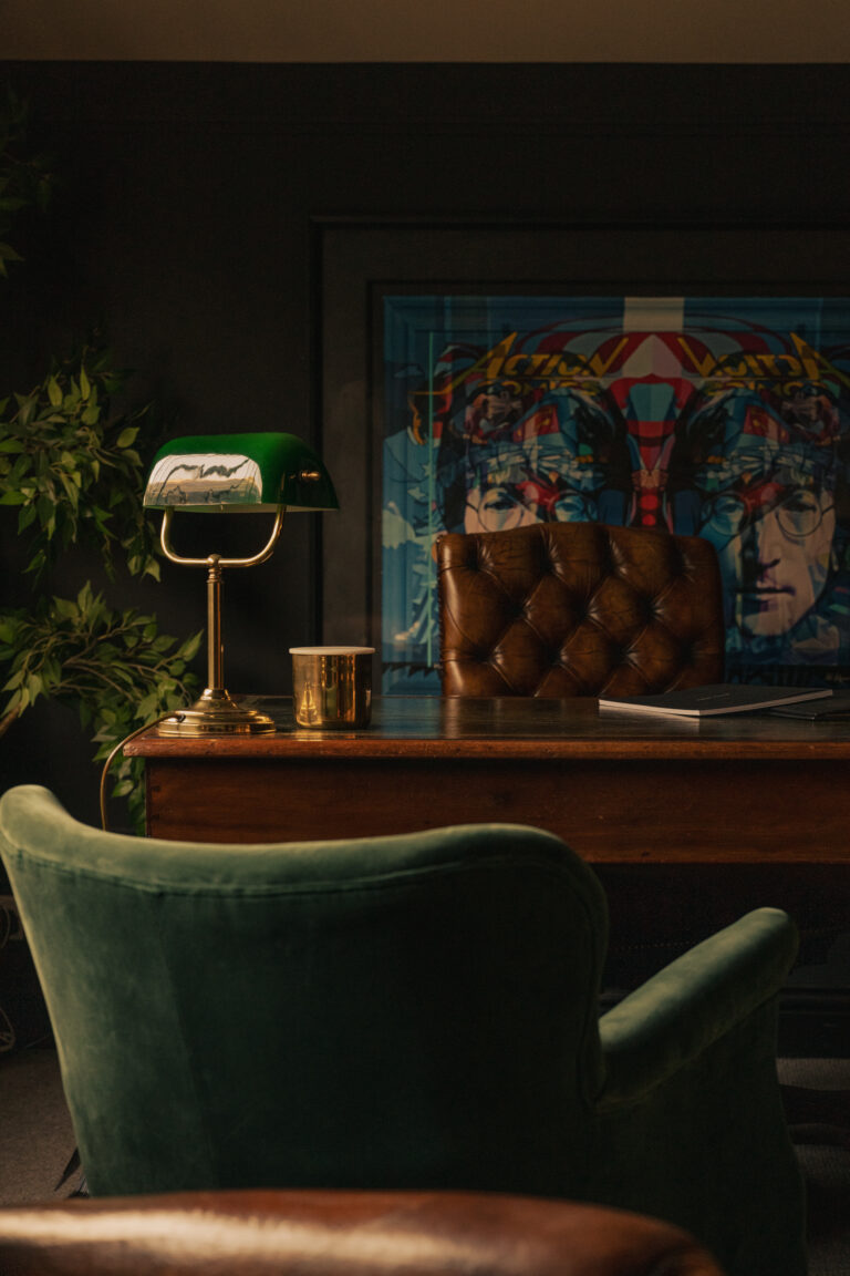 Ralph James office — a warm, characterful workspace with a leather chair, green banker's lamp, and original artwork